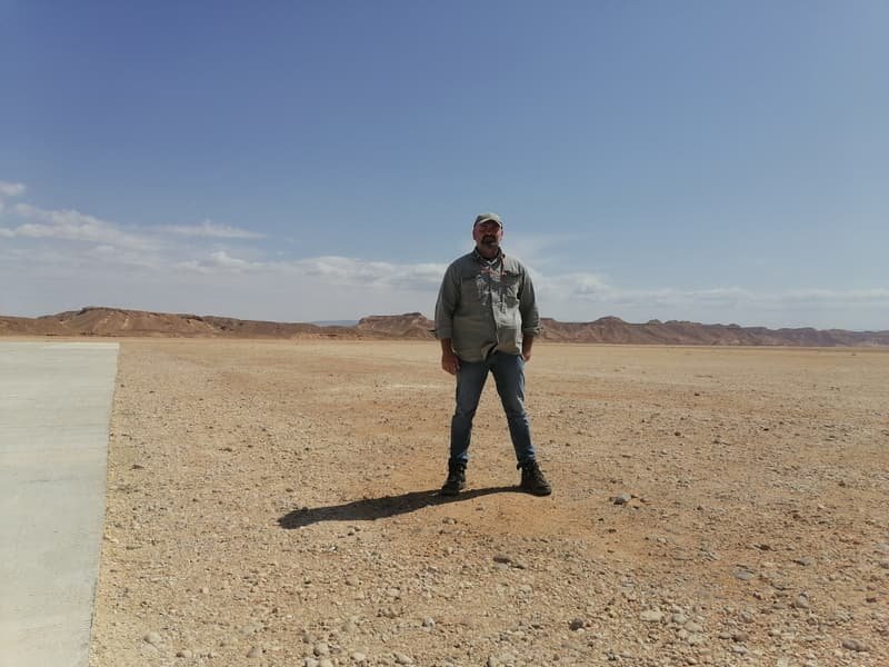 A figure alone on a wide gravel plain, hills on the horizon