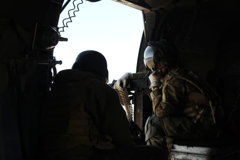 A door gunner silhouetted against the open side of a helicopter