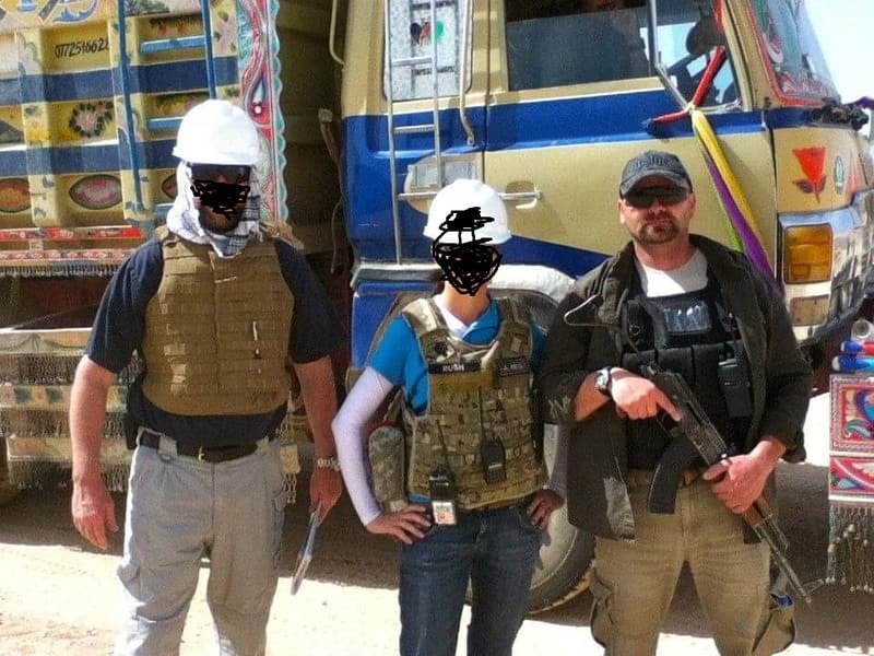 Three members of a close protection team in body armour beside a truck